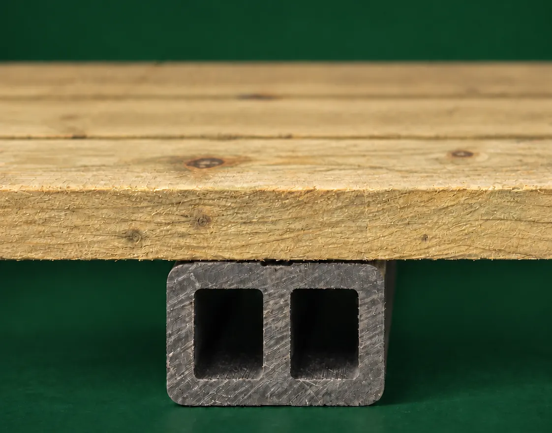 A pressure-treated timber floor board resting on a charcoal composite floor runner, its two hollow chambers visible on the cut end